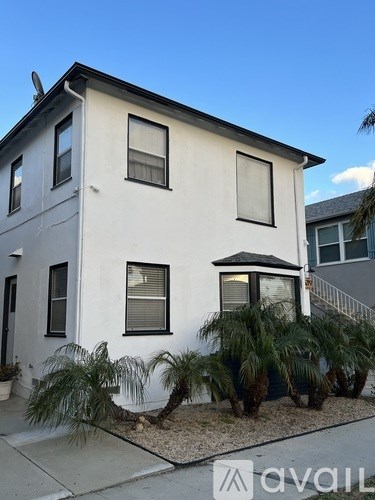 A white two-story house with a black roof and a palm tree in front.