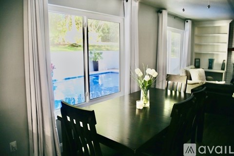 A dining room with a table, chairs, and a view of a pool through the sliding glass doors.