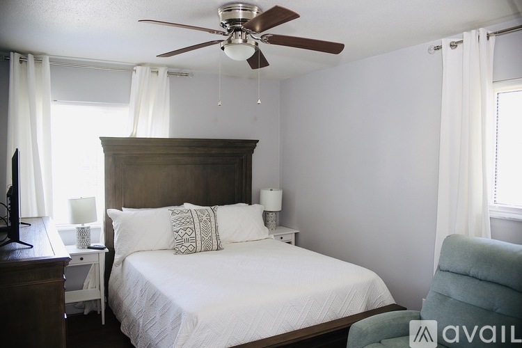 A bedroom with a bed, a ceiling fan, and a chair.