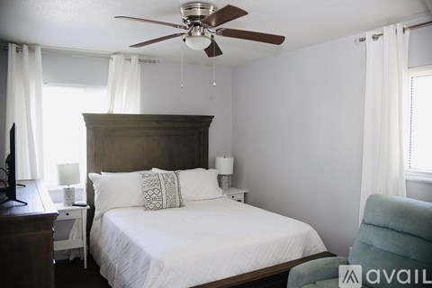 A bedroom with a bed, a ceiling fan, and a chair.