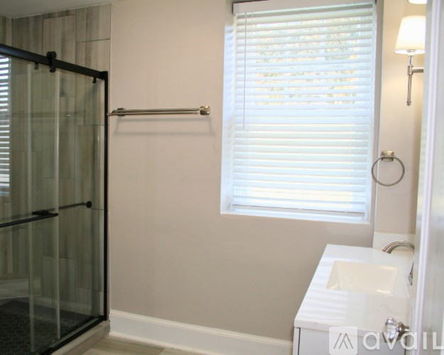 A bathroom with a glass shower door, a sink, and a window with blinds.
