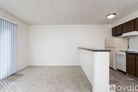 A room with a carpeted floor and a kitchen area in the background.