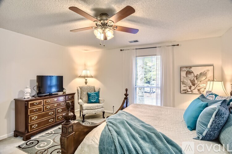 A bedroom with a bed, a dresser, a chair, and a ceiling fan.