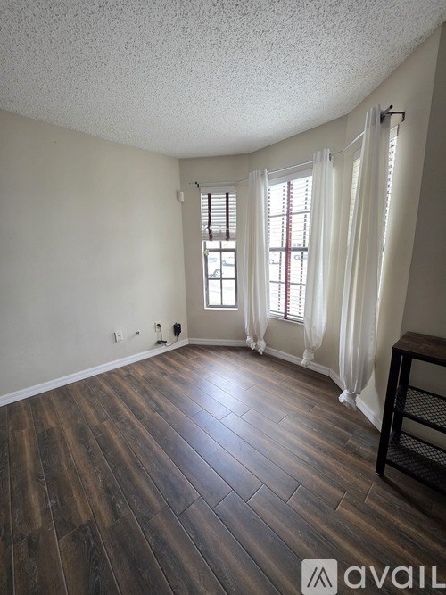 A room with wooden flooring and a window with white curtains.