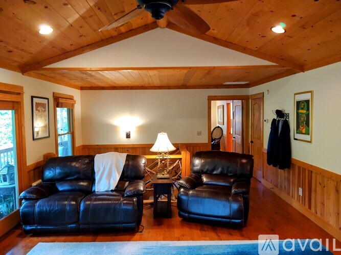 A living room with a black leather couch and a wooden ceiling.