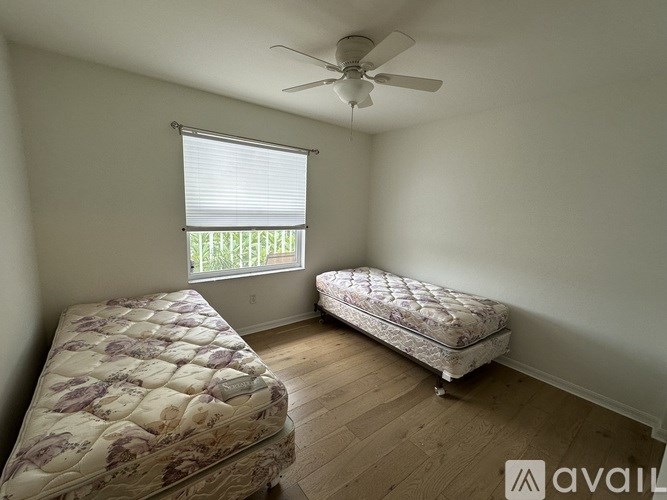 Two twin beds in a room with a ceiling fan and a window with blinds.