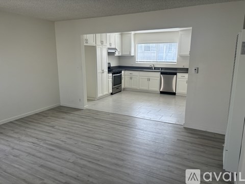 A kitchen with white cabinets and a black countertop is visible from a living room.