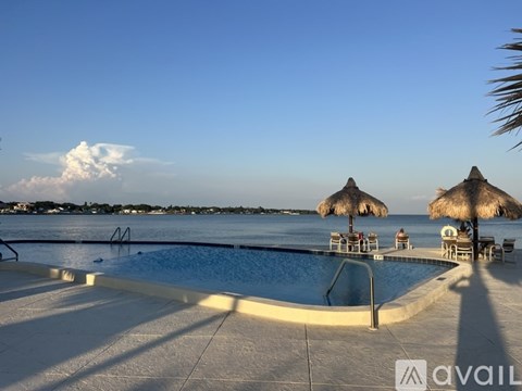 A pool with a sun lounger and umbrella next to a beach.
