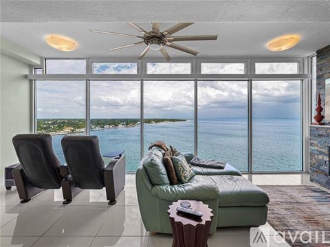 A living room with a green couch and a ceiling fan with a view of the ocean.