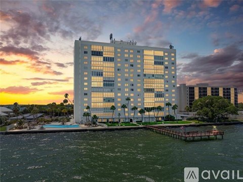 A modern building with a pool in front is surrounded by water and other buildings.