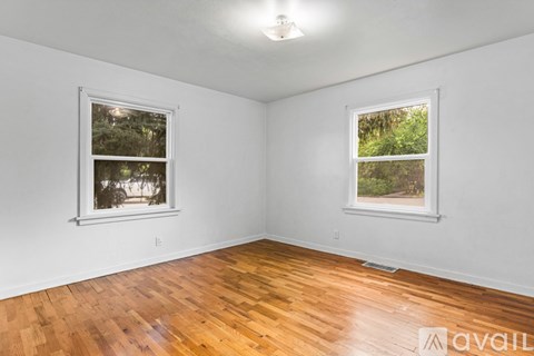 A room with wooden floors and two windows showing trees outside.