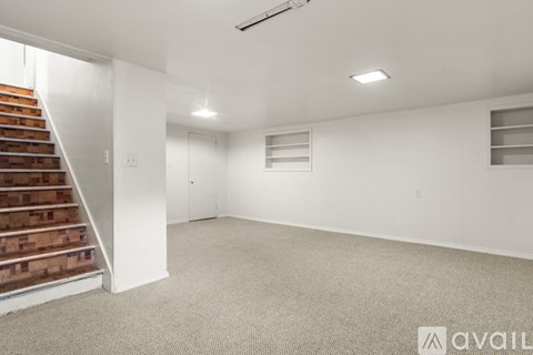 A spacious room with a staircase on the left and a carpeted floor.