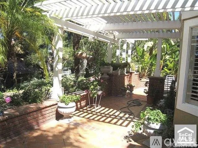 A patio with a white pergola and a table surrounded by plants.