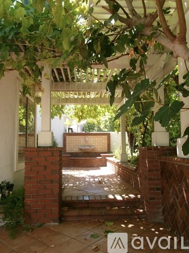 A white pergola with a tree hanging over a brick patio.