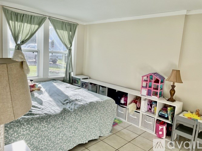 A bedroom with a bed, a window with curtains, and a shelf with toys.