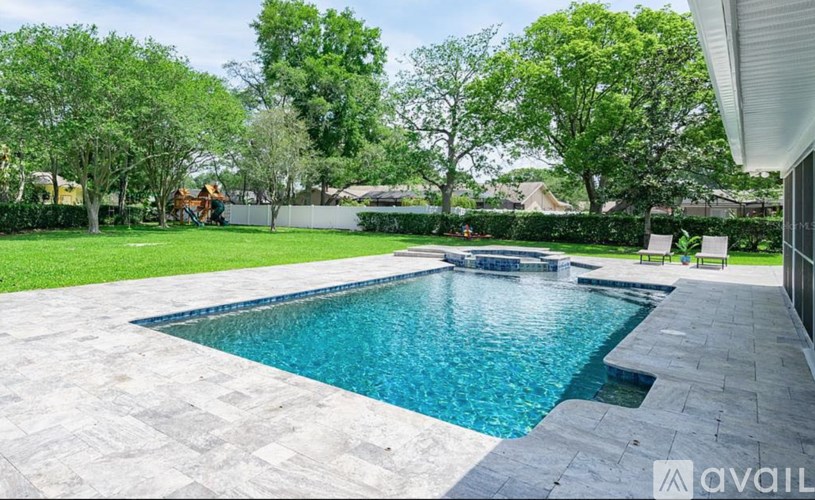 A swimming pool surrounded by a stone patio and a green lawn.