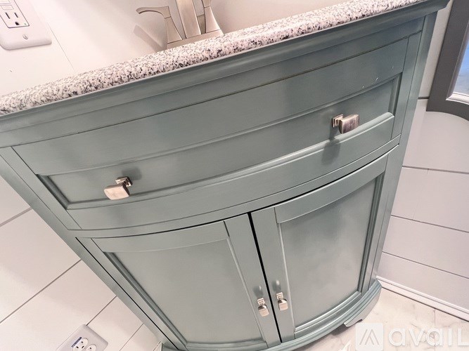 A grey cabinet with a drawer and a door is in a bathroom.