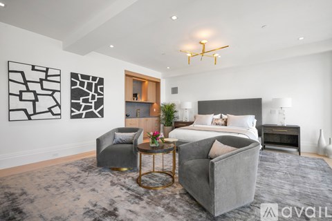 A modern bedroom with a large bed, grey armchairs, and a coffee table.