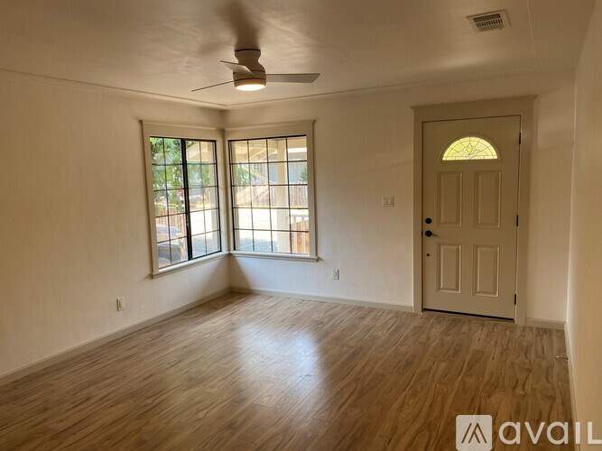 A room with a wooden floor, a ceiling fan, and a door with a glass window.