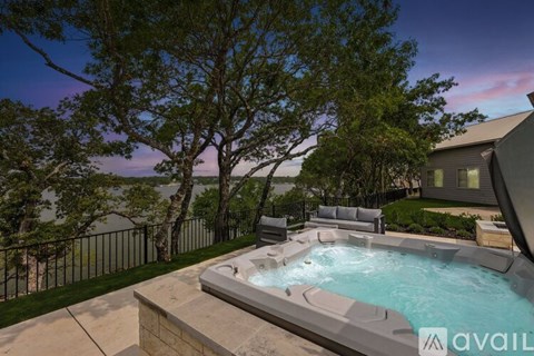 A hot tub is surrounded by a concrete patio and a black fence with trees in the background.