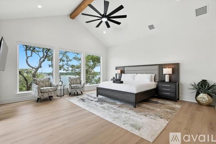 A bedroom with a large bed, a ceiling fan, and a view of the outdoors through the windows.