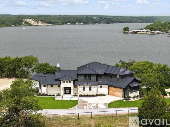 A modern house with a black roof is situated in front of a body of water.