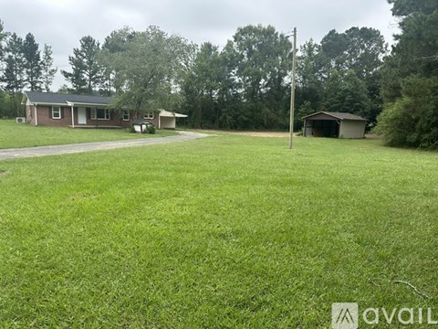 A grassy field with a house and a shed in the background.