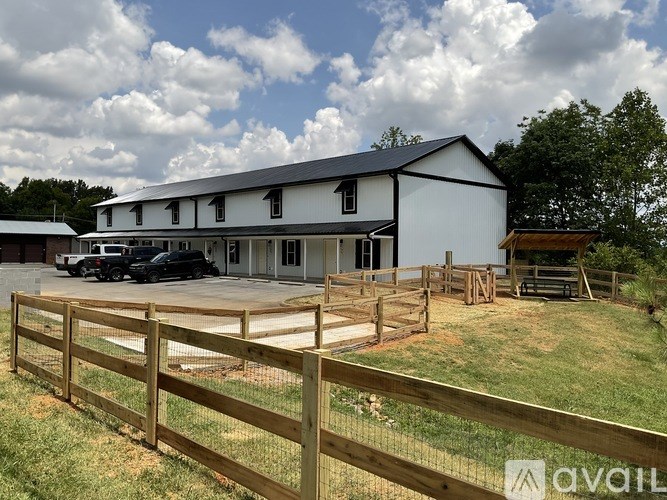 A large white barn with a black roof and a wooden fence in front.