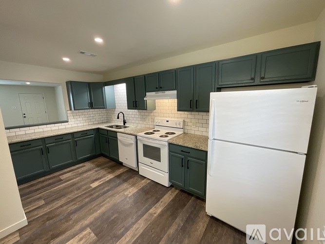 A kitchen with white appliances and dark green cabinets.
