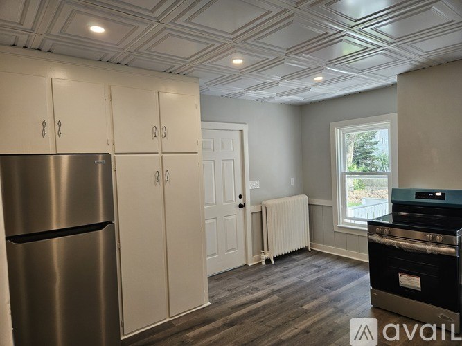 A kitchen with a stainless steel refrigerator, cabinets, and a window.