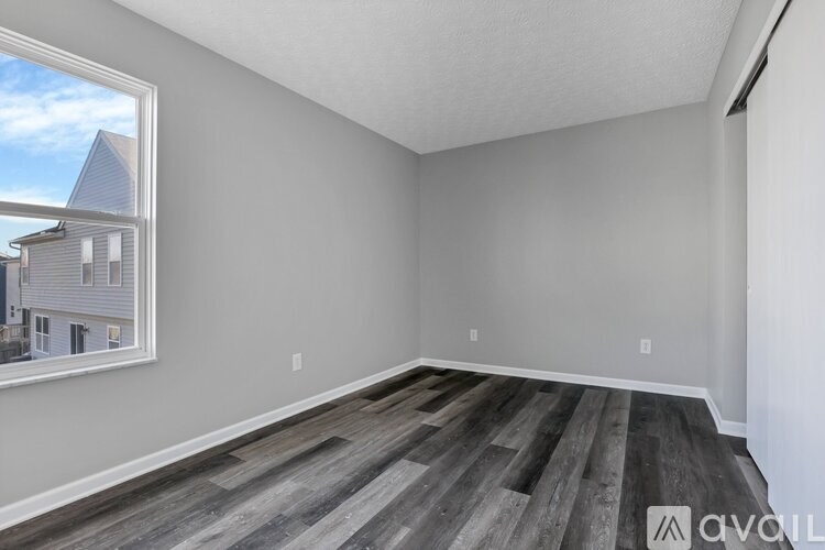 A room with wooden flooring and a window showing a view of a house.