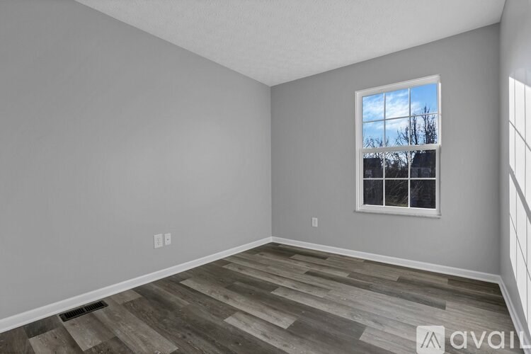 A room with wooden flooring and a window showing a tree outside.