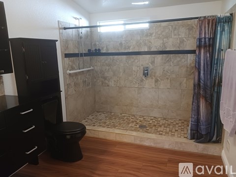 A bathroom with a toilet, a shower with a glass door, and a wooden floor.