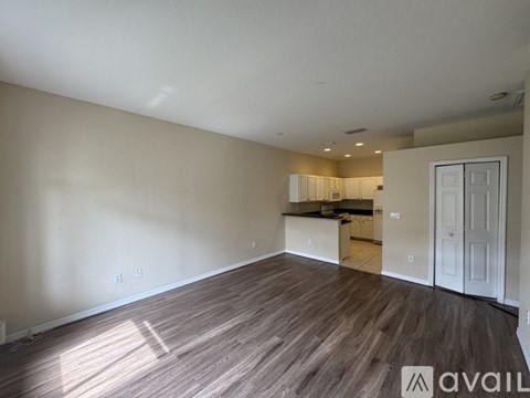 A room with wooden flooring and a kitchen in the background.