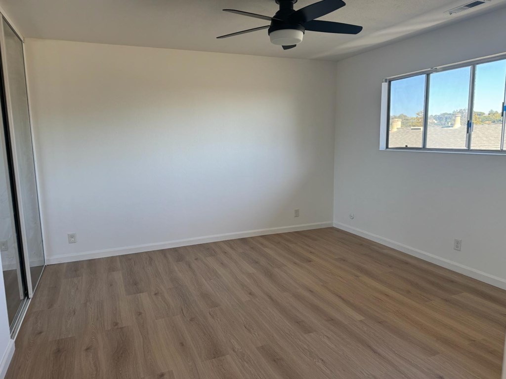 A room with a ceiling fan and a window overlooking a parking lot.