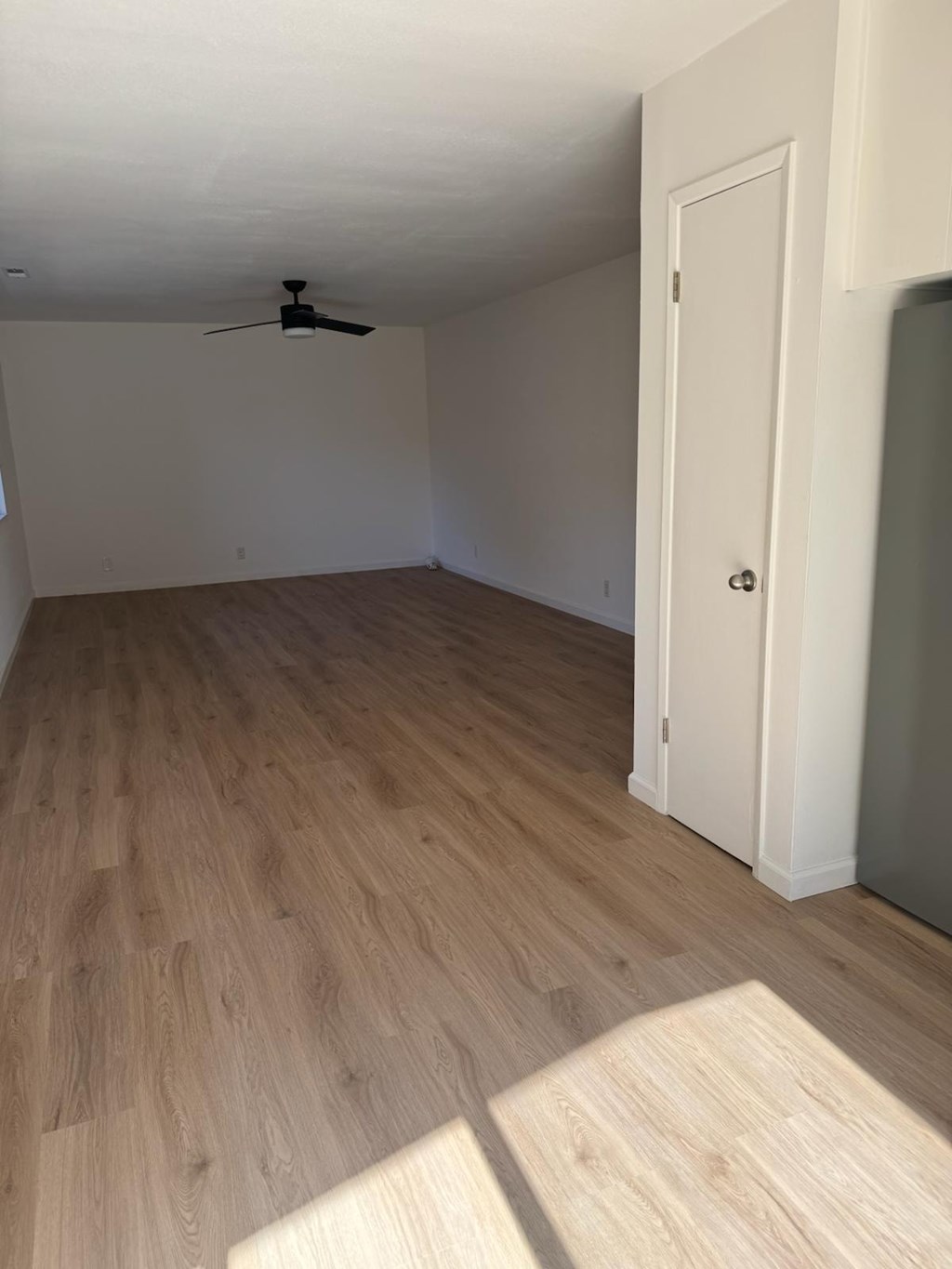 A room with a ceiling fan and light fixture, wooden flooring, and a white door.