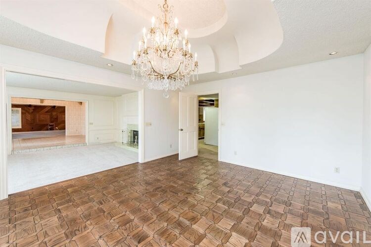 A large empty room with a chandelier and wooden flooring.