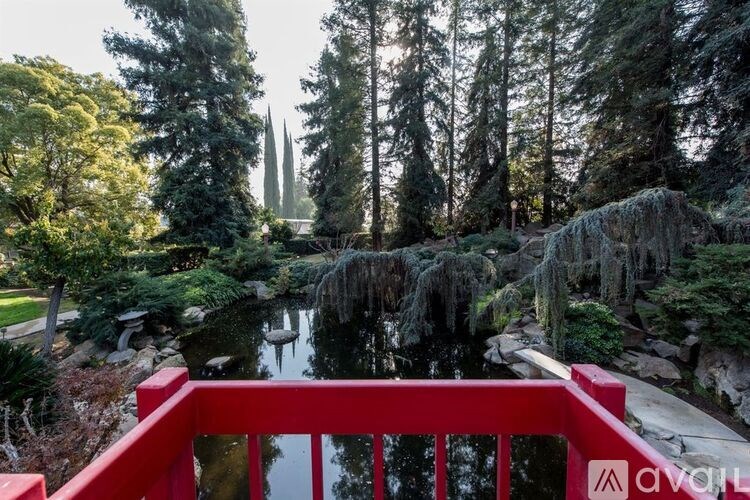 A red bridge leads to a tranquil pond in a lush garden.