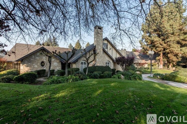 A house with a stone chimney is surrounded by a well-manicured lawn.
