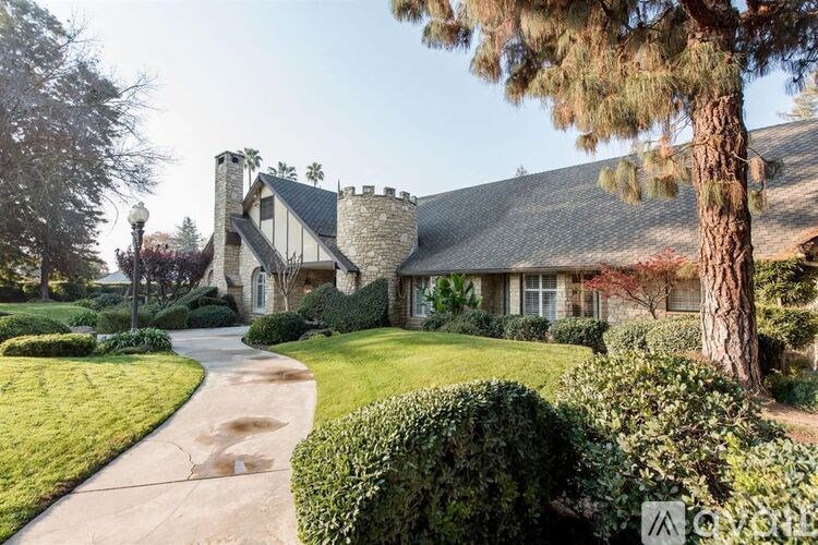 A house with a stone chimney and a pine tree in front.