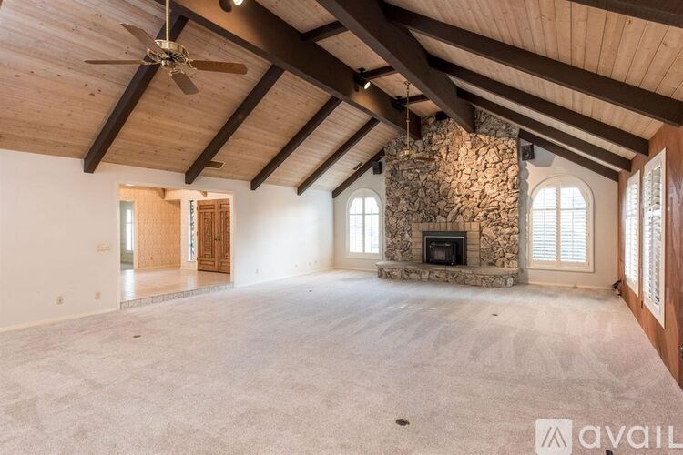 A spacious room with a stone fireplace and wooden beams on the ceiling.