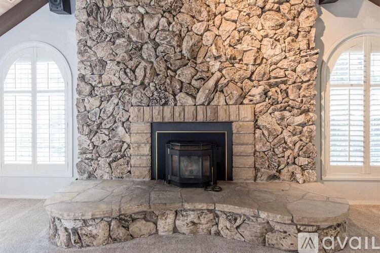 A stone fireplace with a black fireplace insert sits in a room with a stone wall.