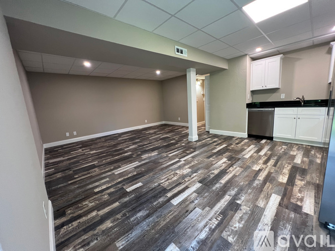 A room with wooden flooring and a kitchenette in the background.