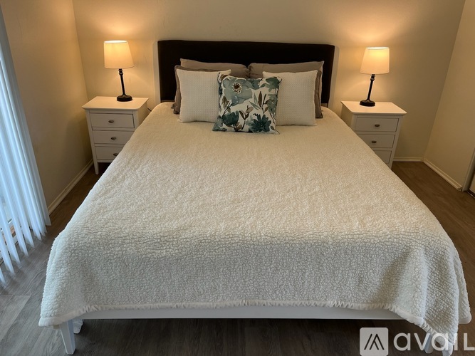A bed with a white comforter and a black headboard with two lamps on the side tables.