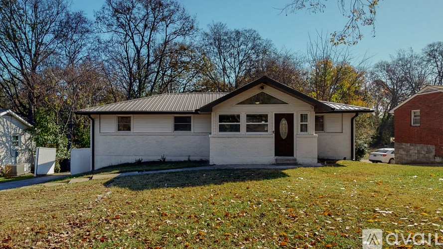 A white house with a brown roof and a brown door is surrounded by trees and grass.