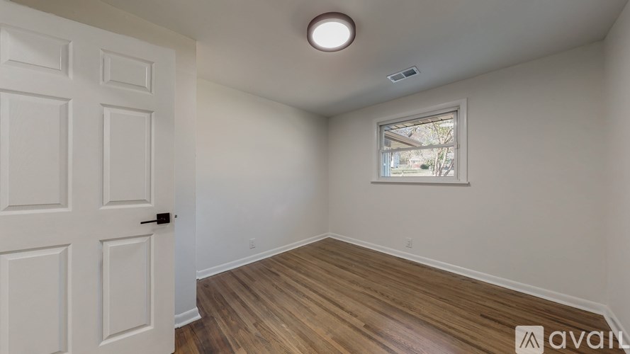 A room with a white door and a window with a view of trees outside.