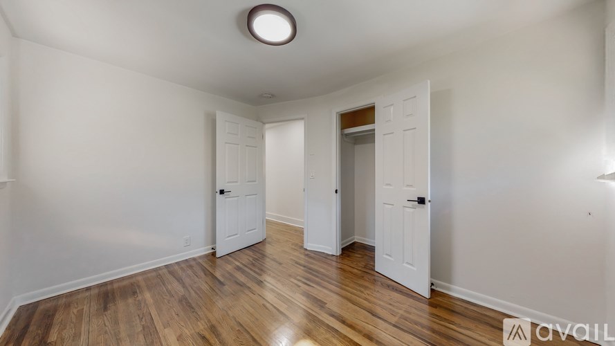 A room with wooden floors and white walls, with a light on the ceiling and a door on the left.