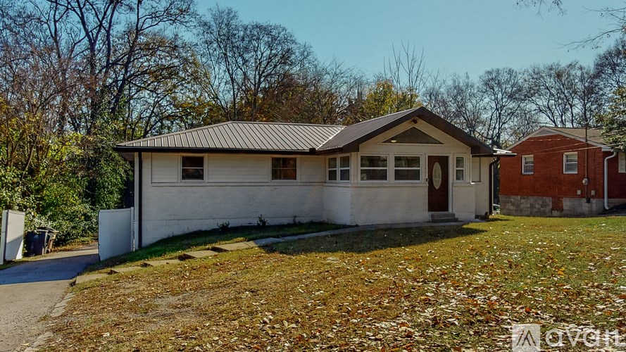 A white house with a brown roof is surrounded by fallen leaves.
