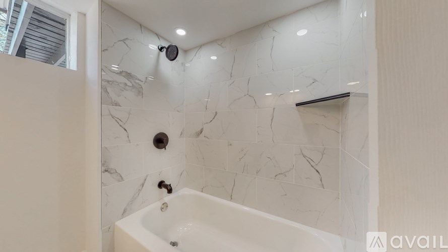 A white bathroom with a marble tile wall and a white bathtub.