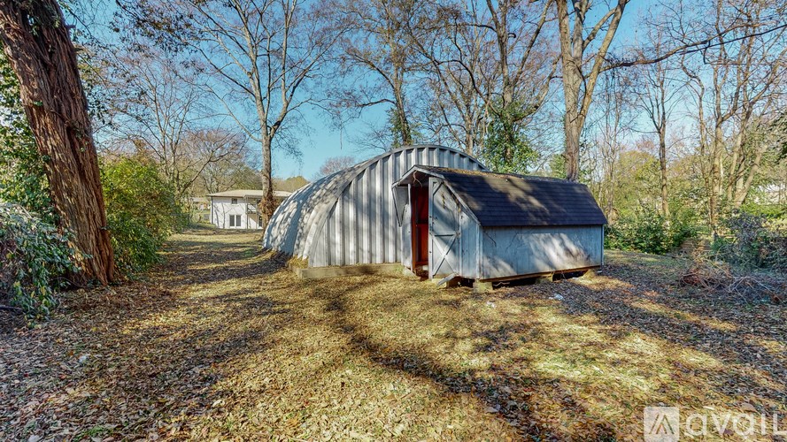 A large, grey, cylindrical building with a red door is situated in a grassy area with trees in the background.